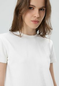 Witte katoenen T-shirt met korte mouwen, ronde hals, gladde textuur en een getailleerd silhouet; geen zichtbare patronen of accenten.