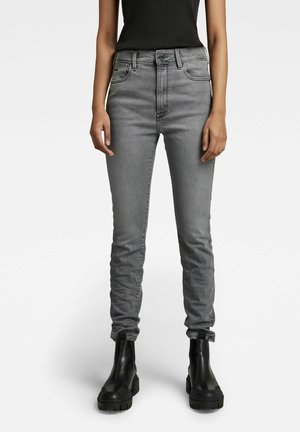 Jeans de talle alto en gris con un corte ajustado, que cuentan con cinco bolsillos, costuras sutiles y cierre de botón; combinados con botas negras de tacón grueso.