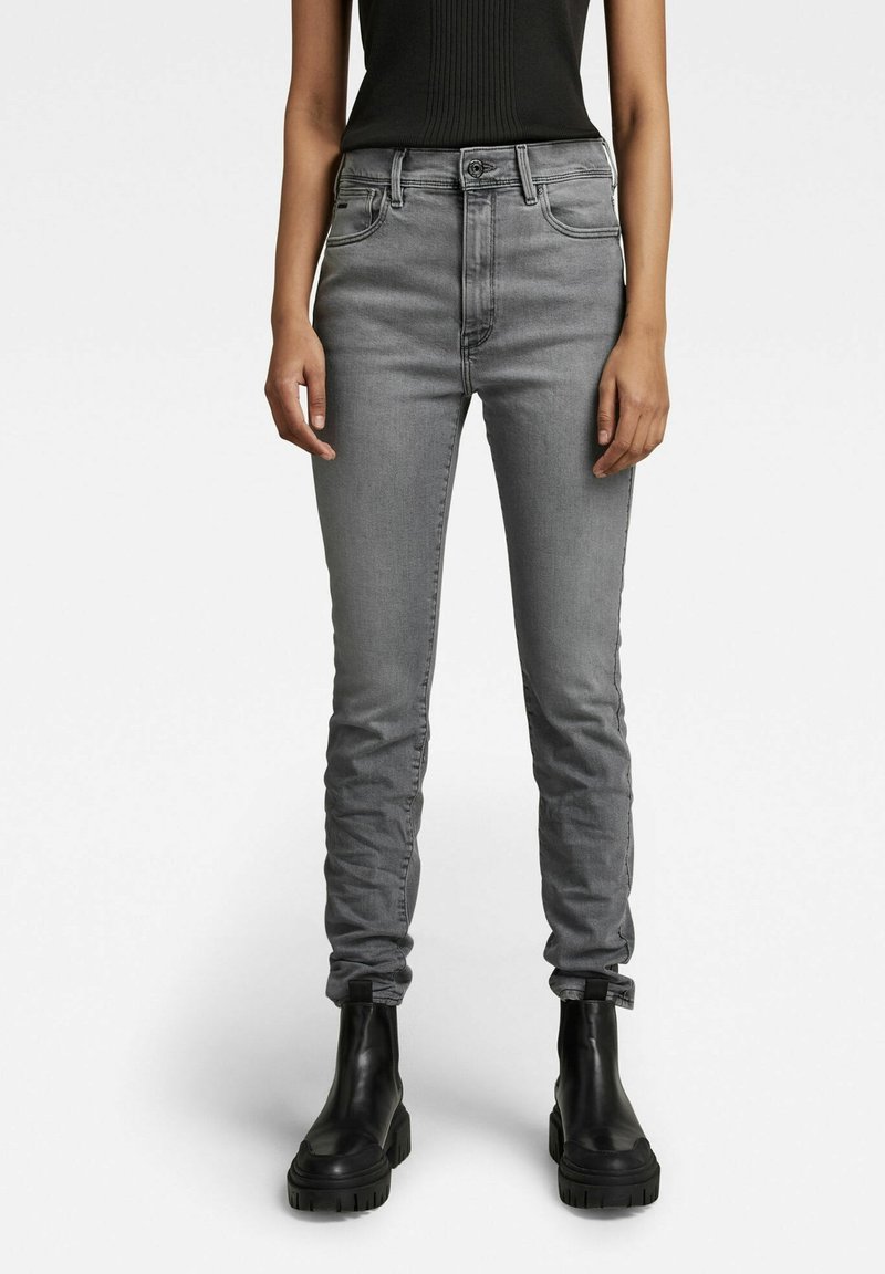Jeans de talle alto en gris con un corte ajustado, que cuentan con cinco bolsillos, costuras sutiles y cierre de botón; combinados con botas negras de tacón grueso.