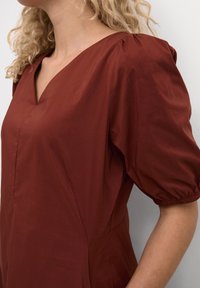 Vyšnių spalvos pūstų rankovių suknelė su V formos iškirpte, pagaminta iš švelnios medžiagos. Turi sukauptas rankoves ir šonines siūles, užtikrinančias pritaikytą siluetą.