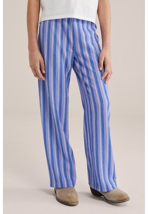 Donna che indossa pantaloni a gamba larga a righe verticali blu, bianche e rosa abbinati a stivaletti beige in suede e una maglietta bianca.