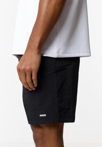 Κοντινό πλάνο ενός ατόμου που φοράει μαύρο σορτς με πλαϊνή τσέπη με φερμουάρ και λευκό κοντομάνικο πουκάμισο.