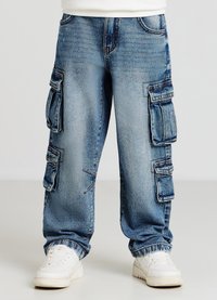 Pantaloni cargo in denim blu chiaro con multiple tasche laterali, vestibilità comoda, finitura sbiadita e orli arrotolati. Abbinati a sneakers bianche.