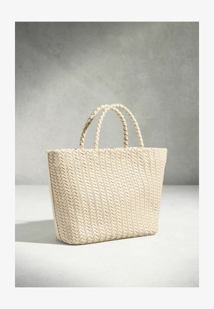 Krēmkrāsas austā tote soma ar divām pīnītām rokturiem, stāv vertikāli uz gaišas virsmas pelēka fona priekšā.