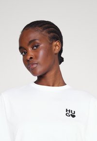 Valge puuvillane T-särk ümmarguse kaelusega ja lühikeste varrukatega. Vasakul rinnal on must "HUGO" logo. Sile tekstuur.