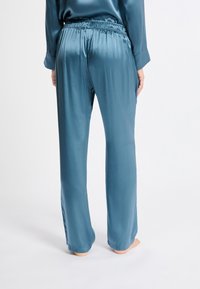 Satijnen pyjamabroek in een teal kleur. Beschikt over een elastische tailleband en een losse pasvorm. Gladde textuur met brede, rechte pijpen.