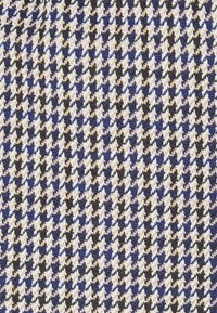 Textil mit einem Hahnentritt-Muster in Marineblau, Beige und Schwarz. Der Stoff zeigt eine gewebte Textur mit kontrastierenden Farben und definierten Formen.