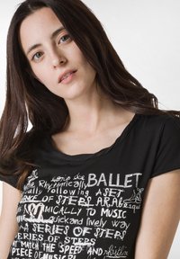 Sort T-shirt med rund hals, prydet med hvid tekst og balletillustrationer, der formidler rytmisk bevægelse og dansebegreber.