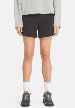 Pantaloni corti neri in cotone con vestibilità aderente, dotati di una fascia elastica in vita, abbinati a un top grigio a maniche lunghe e scarpe da ginnastica grigie e viola.