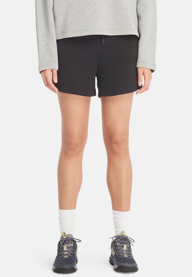 Sorte bomuldsshorts med en tætsiddende pasform, udstyret med en elastisk talje, parret med en grå langærmet top og grå-lilla sportsko.