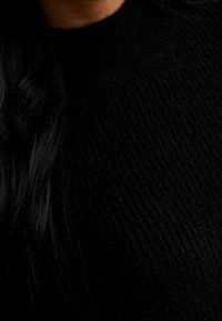 Maglione nero lavorato a maglia con un design testurizzato a coste e un collo alto, realizzato in un materiale morbido e accogliente.