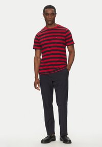 T-shirt a maniche corte a righe rosse e blu, scollo rotondo, con un piccolo logo, abbinata a pantaloni e scarpe nere.