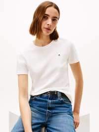 T-shirt branca de algodão com mangas curtas, gola redonda e um pequeno logotipo no peito. Combinada com jeans de ganga azul de cintura alta.