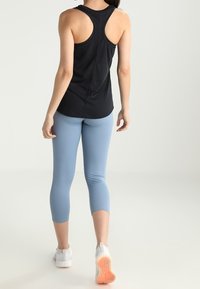 Czarny top na ramiączkach z plecami w kształcie litery racer, zestawiony z jasnoniebieskimi legginsami capri i białymi butami sportowymi, ukazując gładki materiał i dopasowany krój.