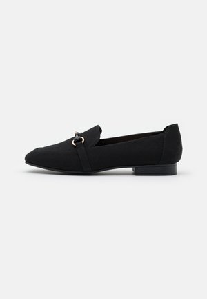 Mocassins en toile noire avec un bout arrondi, un petit talon bloc, et une bride décorative avec un accent doré. Texture lisse et design minimaliste.