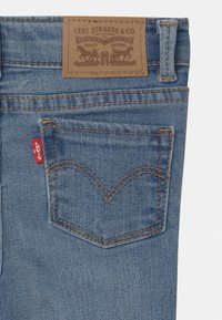 Vaqueros de mezclilla azul con una etiqueta de cuero que presenta "Levi Strauss & Co." en la cintura, una pequeña etiqueta roja y costuras distintivas en el bolsillo trasero.