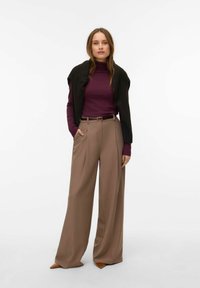 Kõrge vöökohaga beežid laia säärega püksid esisoojendustega, mis on kombineeritud keha järgiva lilla kaelusega ja musta šaaliga, mis on üle õlgade laotatud.