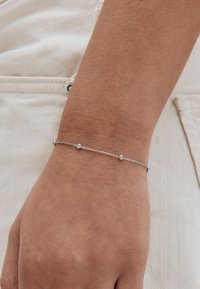 Srebrna bransoletka z łańcucha z małymi okrągłymi akcentami, noszona na nadgarstku, o delikatnym wzorze i gładkiej fakturze na skórze.