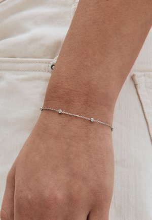 Hõbedane kettkäevõru väikeste ümmarguste aksentidega, kantud randmel, omades peent disaini ja siledat tekstuuri naha vastu.