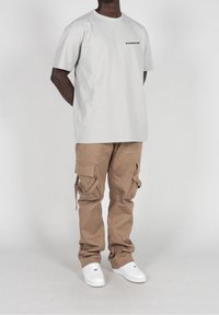 Lys grå bomulds T-shirt med sort logo, parret med tan cargobukser, der har flere lommer og justerbare stropper, båret med hvide sneakers.