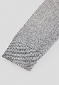 Szary, dzianinowy rękaw swetra z prążkowanym mankietem, charakteryzujący się gładką fakturą i subtelnymi wariacjami kolorystycznymi. Czysty, minimalistyczny design.