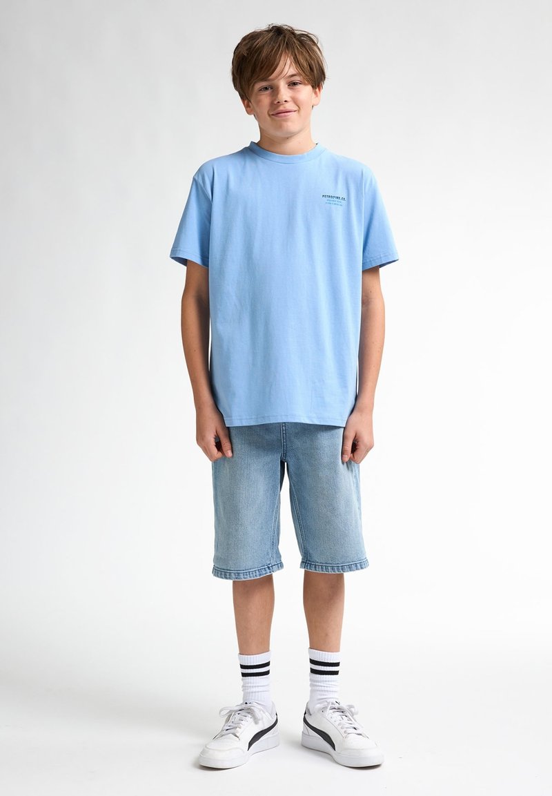 T-shirt en coton bleu clair, short en denim, baskets blanches avec accents noirs et chaussettes blanches rayées. Coupe décontractée, design simple, sans motifs.