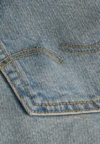 Modra denim tkanina z zašito žepom z ukrivljenim vrhom, okrašena z kontrastnim rumenim šivom in subtilnimi različicami v strukturi.