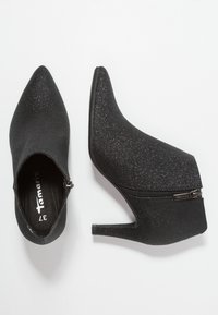 Stivaletti neri brillanti alla caviglia con punta appuntita, chiusura con zip coperta e tacco sottile. Texture liscia con una finitura luccicante.