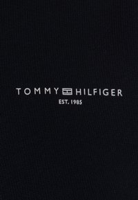 Czarna tkanina o fakturowanym splocie z białym logo marki "TOMMY HILFIGER" oraz napisem "EST. 1985" wydrukowanym poniżej.
