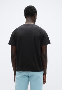 Μαύρο κοντομάνικο t-shirt με στρογγυλή λαιμόκοψη και μανίκια ράγκλαν, κατασκευασμένο από απαλό βαμβακερό ύφασμα. Διαθέτει ίσια ραφή στο κάτω μέρος και λιτή λεπτομέρεια.