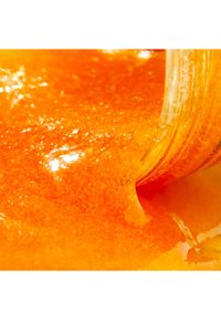 Gyllengul orange gel med en slät, glansig yta som visar en tjock konsistens när den rinner ut från en burk och framhäver ljusreflektioner.