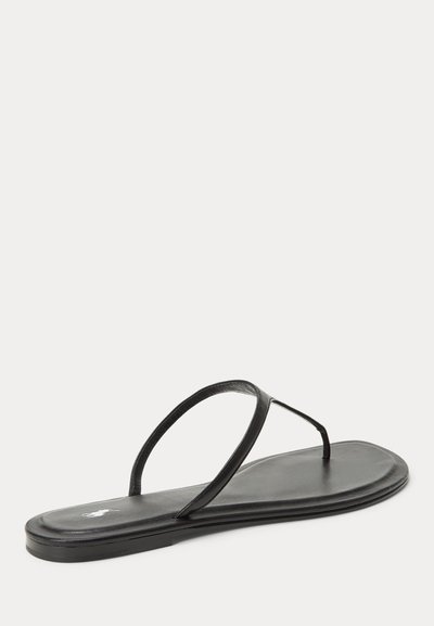 Μαύρο επίπεδο σανδάλι με λεπτά δερμάτινα λουριά, θηλιά για το δάχτυλο και χαμηλό τακούνι, εμφανίζεται σε ανοιχτό φόντο.