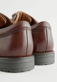 Chaussures en cuir marron avec des coutures visibles et une finition lisse. Présentent une semelle en caoutchouc noir contrastante avec un profil texturé.