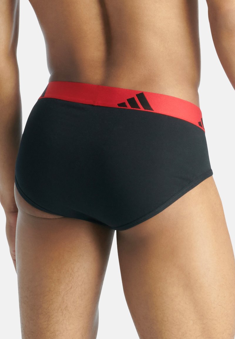 Slip neri con una vita elastica rossa che presenta accenti del logo Adidas nero. Tessuto liscio con un design aderente.