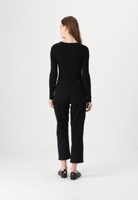 Zwarte geribbelde lange mouwen top gecombineerd met hoge taille zwarte jeans. Model staat met de rug naar de camera, met een fitted stijl en minimalistische ontwerpdetails.