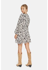 Vestido beige de manga corta con estampado de leopardo negro, falda acampanada y cintura ceñida. Combinado con botas marrones hasta la rodilla.