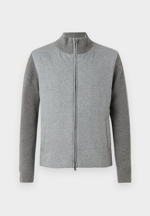 Giacca grigia con zip, caratterizzata da un frontale liscio e maniche a costine. Collo alto e tasche laterali, progettata con una silhouette semplice e moderna.