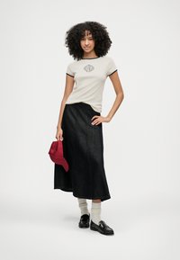 Tricou crem cu margine neagră, detaliu grafic; fustă lungă din denim închis; șapcă roșie; loafers negri; ciorapi albi cu dungi. Outfit simplu, casual.