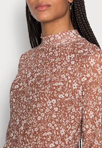 Brun blommönstrad klänning med hög hals och långa ärmar i ett lätt, texturerat tyg.