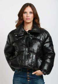 Giacca a vento nera con texture lucida e trapuntata, grande colletto, zip frontale e chiusura con bottoni a pressione; presenta tasche laterali e design accorciato.