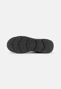 Schwarze Sneaker-Sohle mit hexagonalem Profil und segmentierten Rillen für Flexibilität, vor einem schlichten weißen Hintergrund gezeigt.