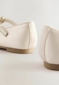 Beige Satin-Ballerinas mit abgerundetem Zehenbereich und kleinem Absatz. Mit einem dünnen metallischen Riemen und dezenten Nähten. Glatte Textur.