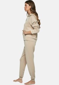 Beige hoodie met een kangoeroezak, gecombineerd met bijpassende taps toelopende joggingbroeken. Zacht materiaal met geribbelde manchetten, zijnaden en een relaxte fit.