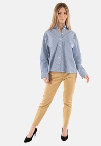 Camisa de botones a rayas azul y blanca con un solo bolsillo en el pecho, combinada con pantalones beige ajustados y tacones altos negros.