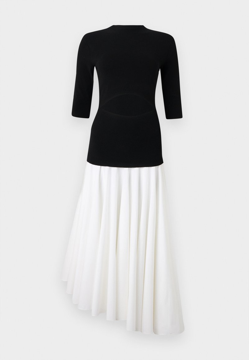 Schwarzes Strickoberteil mit 3/4-Ärmeln, kombiniert mit einem weißen, asymmetrisch fallenden Plissiertenrock, der einen kontrastierenden zweifarbigen Effekt erzeugt.