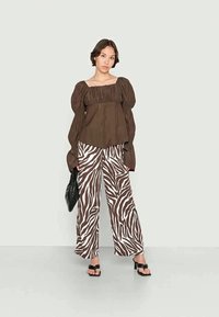 T-shirt castanho com mangas bufantes e textura pregueada, combinada com calças largas listradas em zebra brancas e castanhas. Mala preta, sandálias rasas.