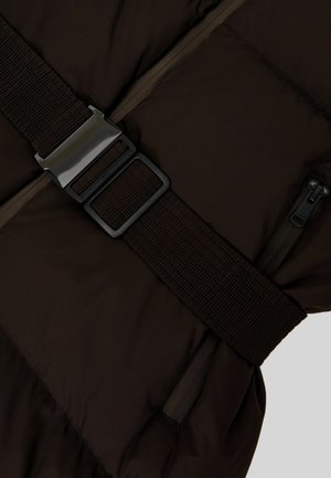 Rudas paminkštintas liemenė su plačia tekstūruota juoda dirželiu ir metaline sagtimi, su įstrižomis užtrauktukinėmis kišenėmis abiejose pusėse.