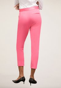 Roze op maat gemaakte broeken met een gladde textuur, een cropped lengte en een achterzakdetail, gedragen met zwarte gepatineerde hakken.