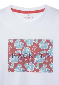 Maglietta bianca in cotone con una stampa floreale rettangolare nei toni del blu e del rosso, con "HACKETT LONDON" in testo blu scuro al centro.