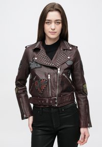 Bordó bőrmotoros dzseki ezüst szegecsekkel, finoman kidolgozott foltokkal, derékban övvel és cipzáras mandzsettákkal. Díszítő elemekkel ellátva.